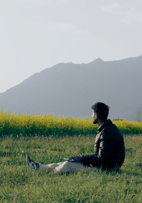 一名男子坐在田野里，手里拿着笔记本电脑