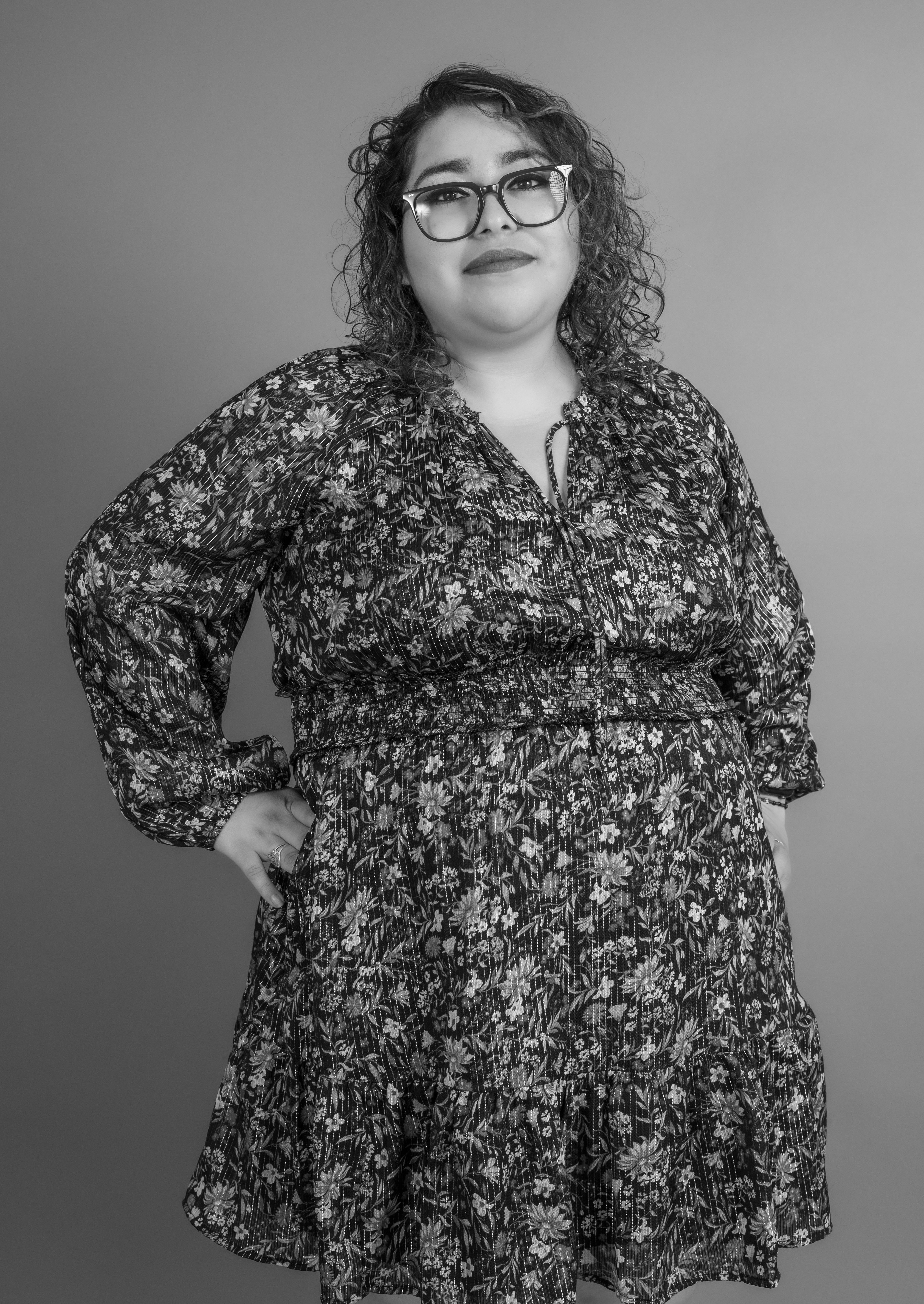 Stylish black and white portrait of a woman in eyeglasses and a floral dress, captured in a studio.