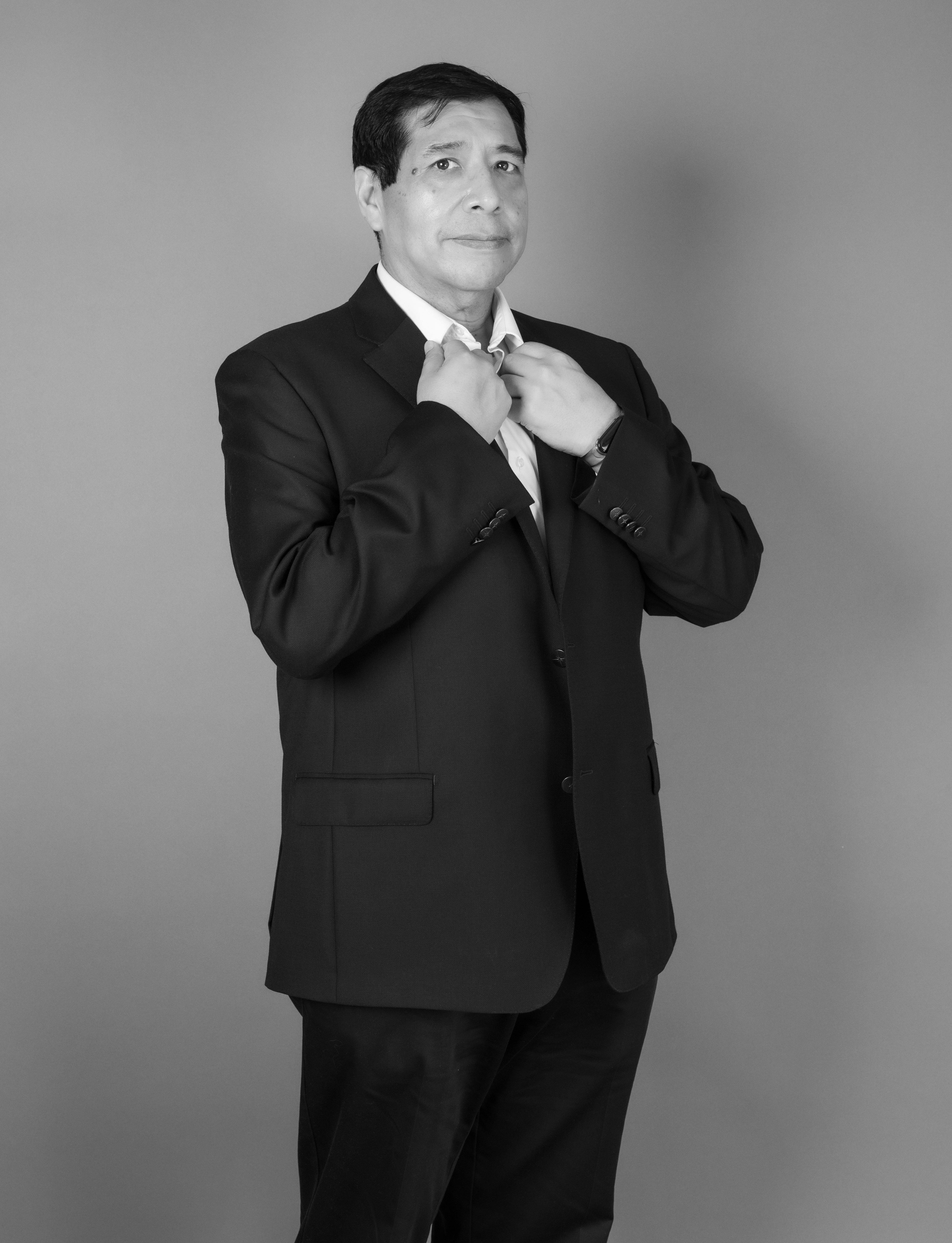 Black and white portrait of a confident middle-aged man in a suit, adjusting his tie.