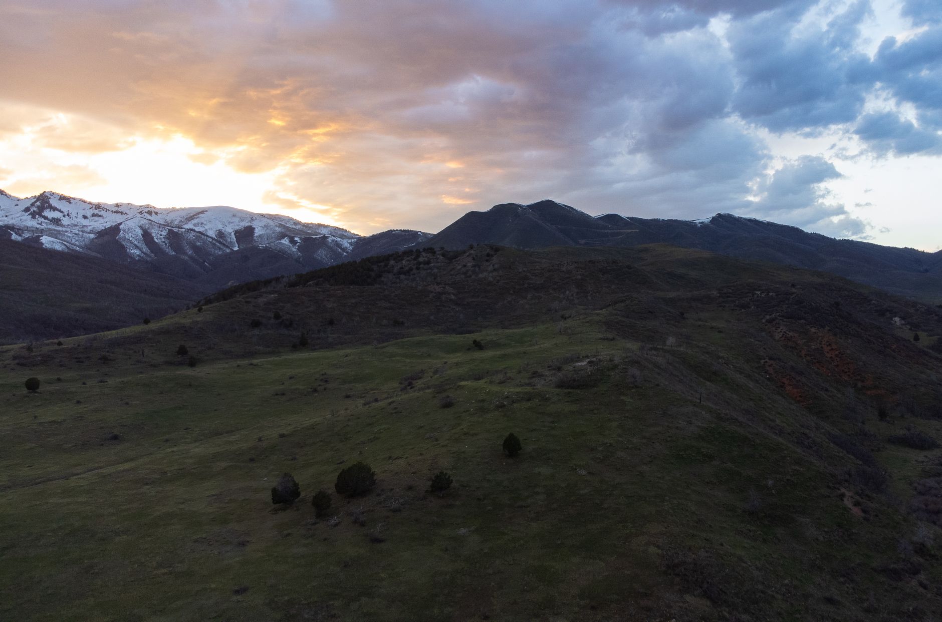 A scenic view of the Spanish Fork mountains at sunset with clouds and a tranquil meadow.