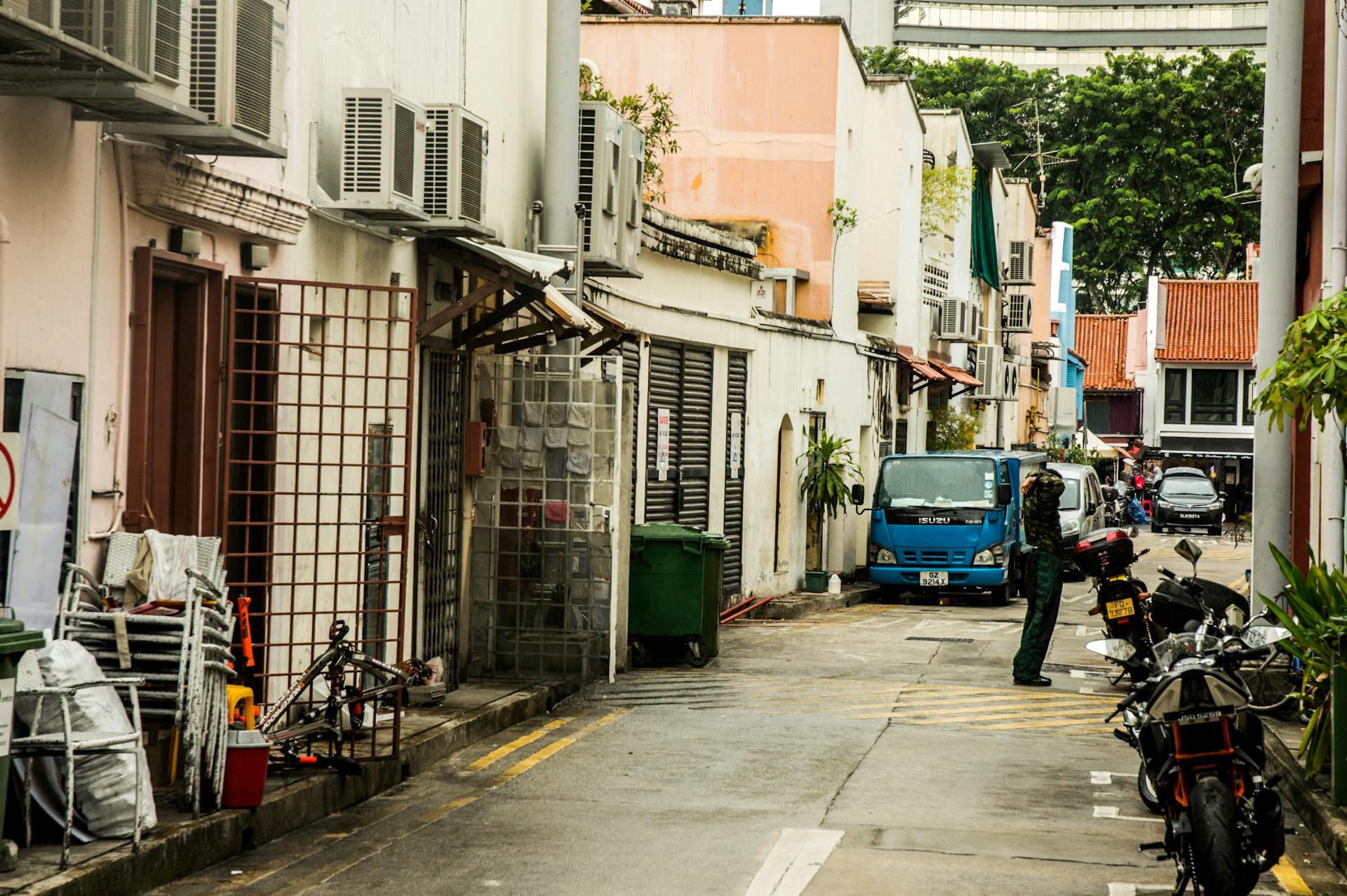 A vibrant Singapore street scene featuring parked vehicles, buildings, and a person.