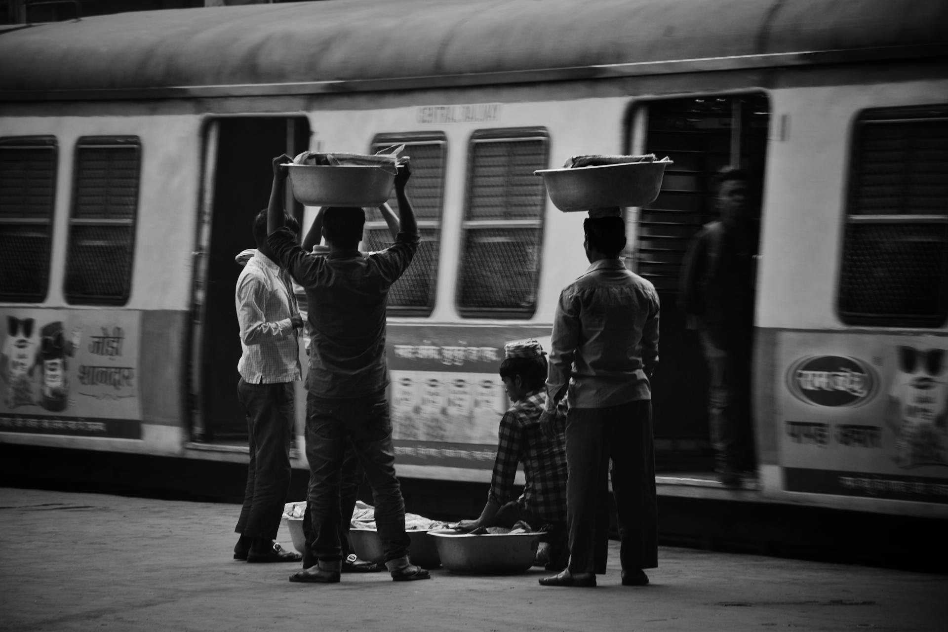 Street vendors with tubs waiting by Mumbai local train, capturing daily life.