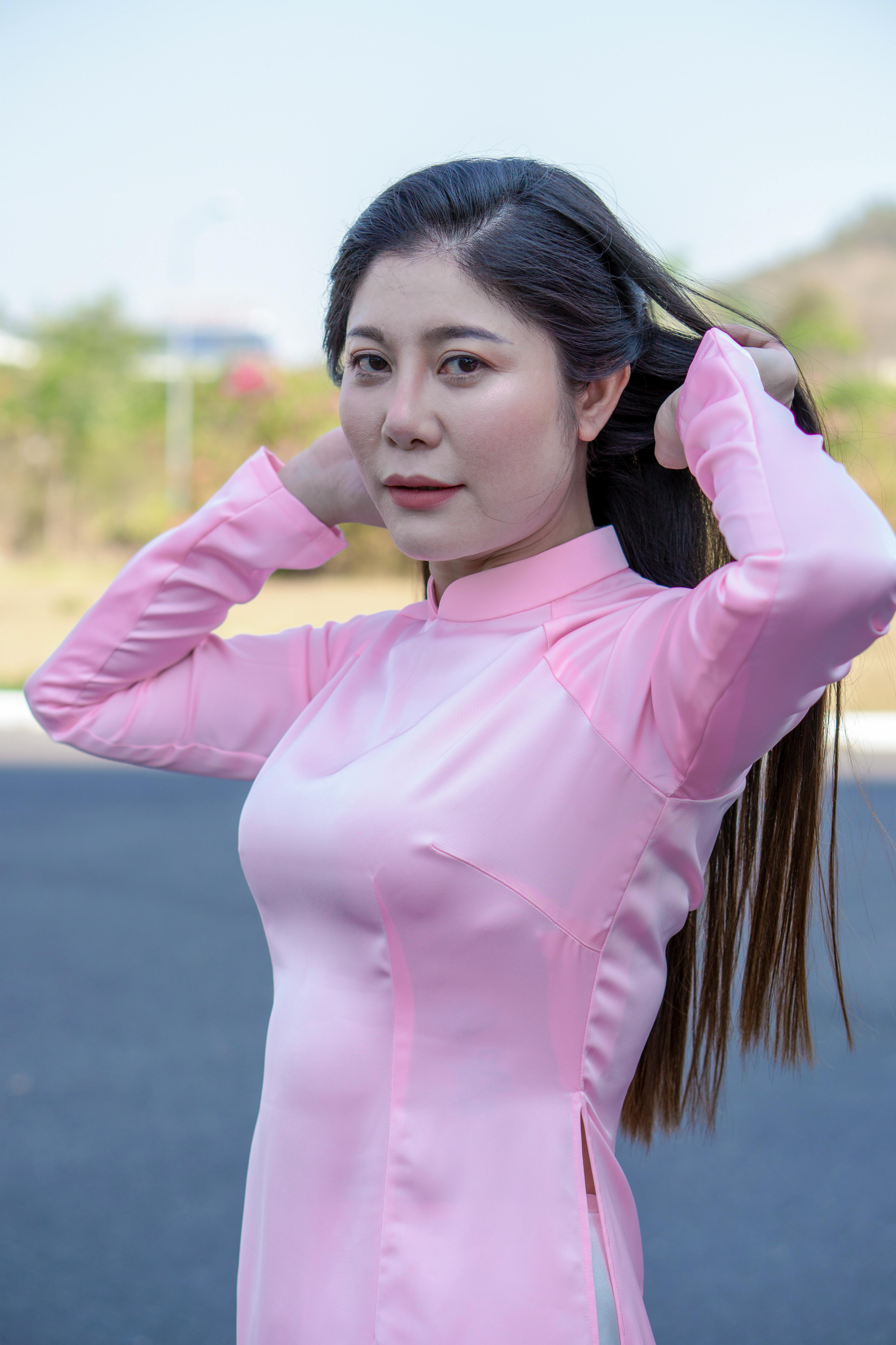 Portrait of a woman in a pink traditional dress fixing her hair outdoors on a sunny day.