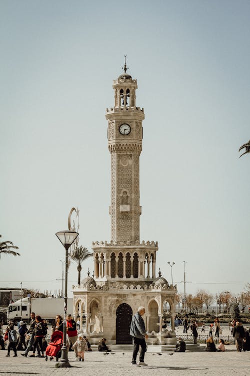 A clock tower in a plaza with people walking around