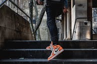 在城市环境中，一个人穿着时尚的橙色和白色运动鞋爬户外楼梯