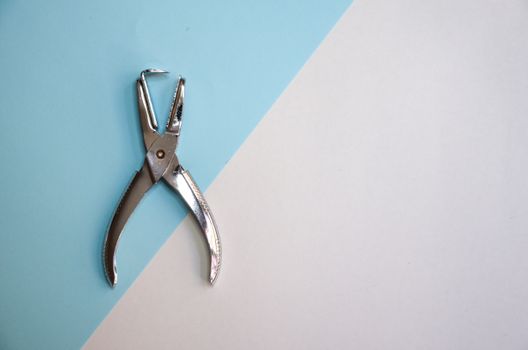A pair of stainless steel pliers placed on a minimalist blue and white backdrop.