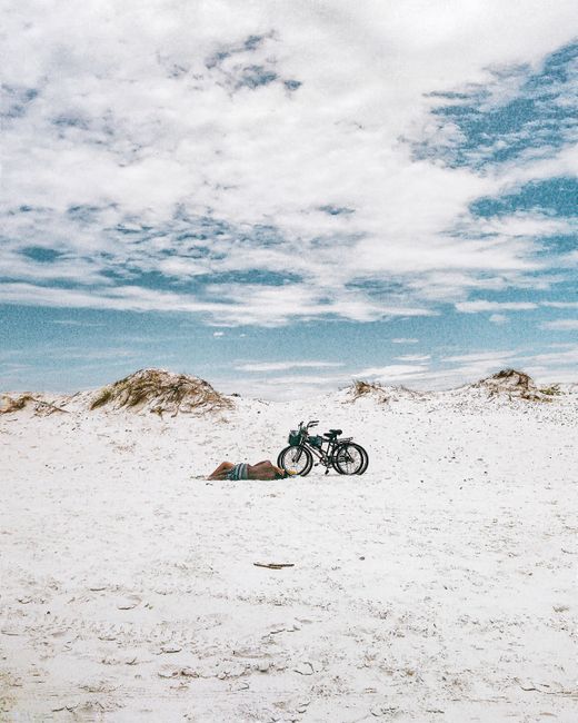 Two bicycles on a vast sandy beach under a clear blue sky, capturing a serene, summer vibe.