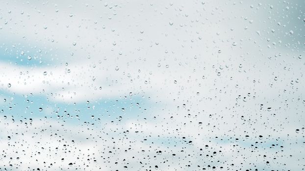 Clear raindrops on a window with a blue and cloudy sky in the background.