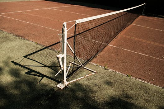 Close-up of a tennis net on a deserted court with rich shadows and sunlight.