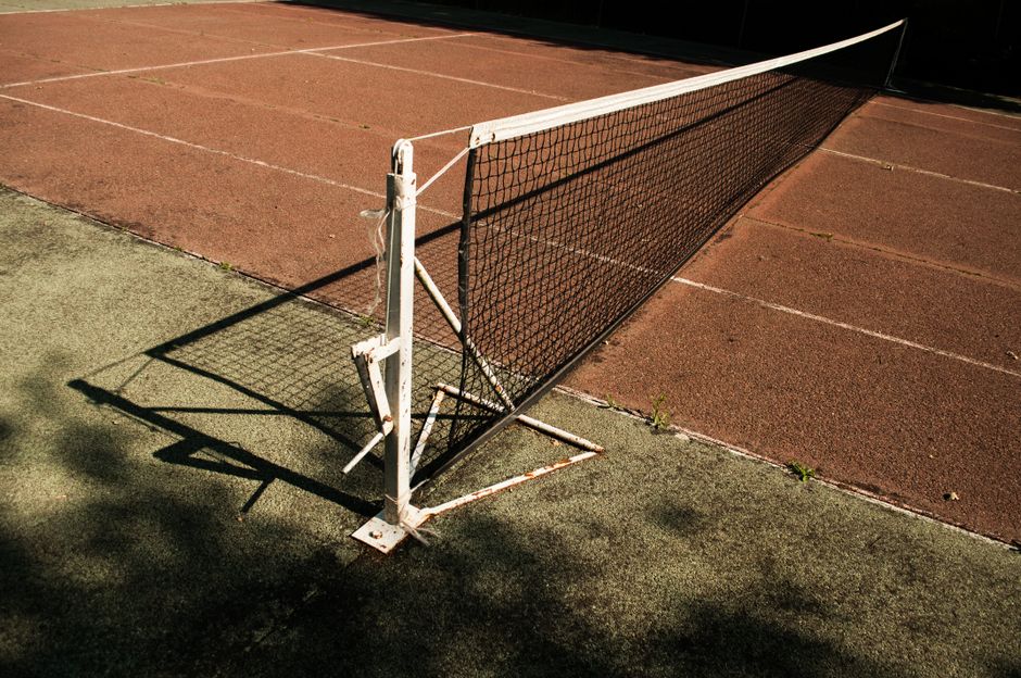 Close-up of a tennis net on a deserted court with rich shadows and sunlight.