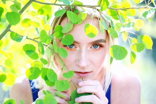 A close-up portrait of a woman with blonde hair, surrounded by green leaves outdoors.
