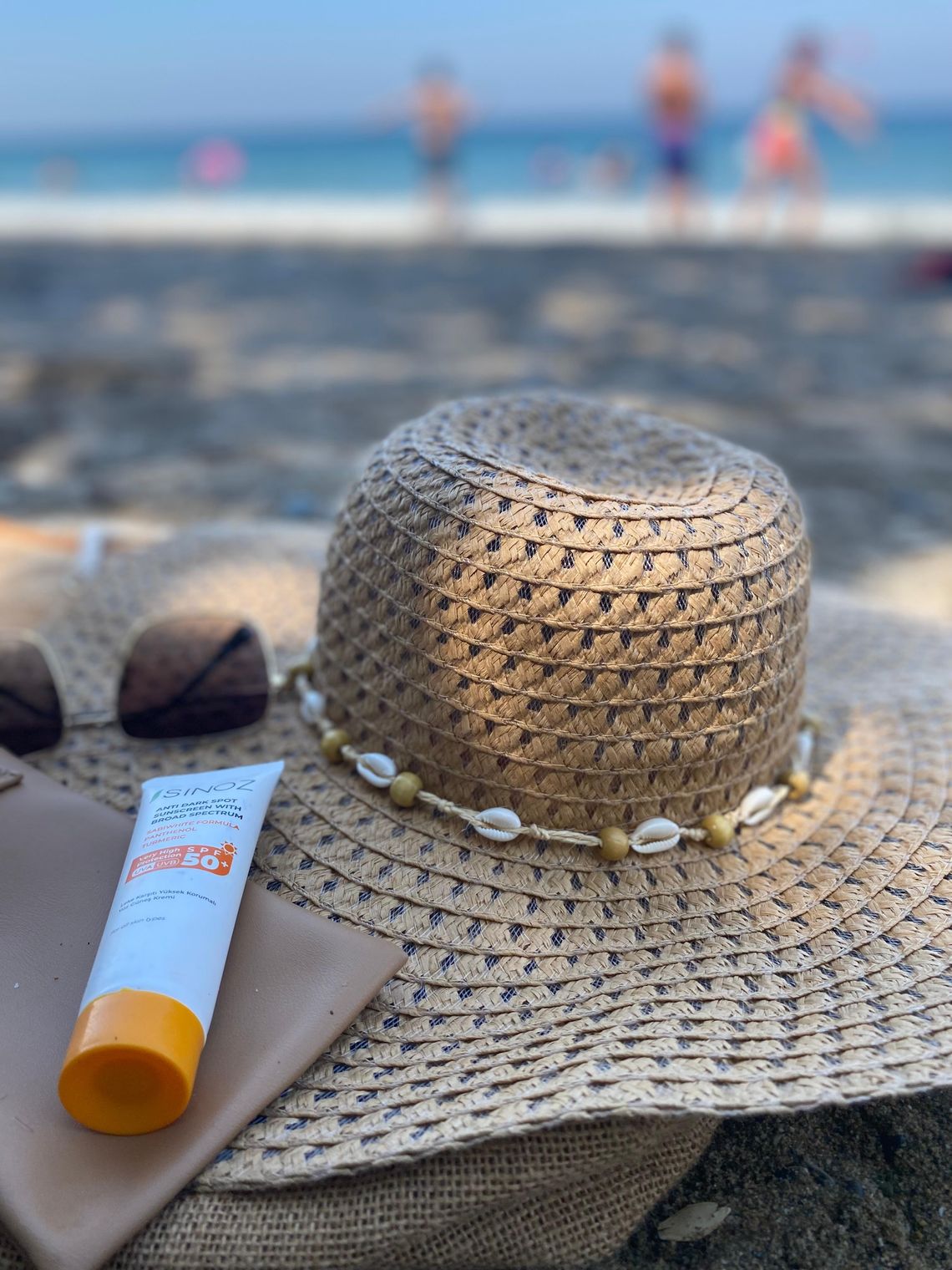 Straw hat and sunscreen arranged on a sandy beach