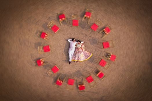 A unique aerial photo of a couple lying in a circle of red chairs, symbolizing unity and love.