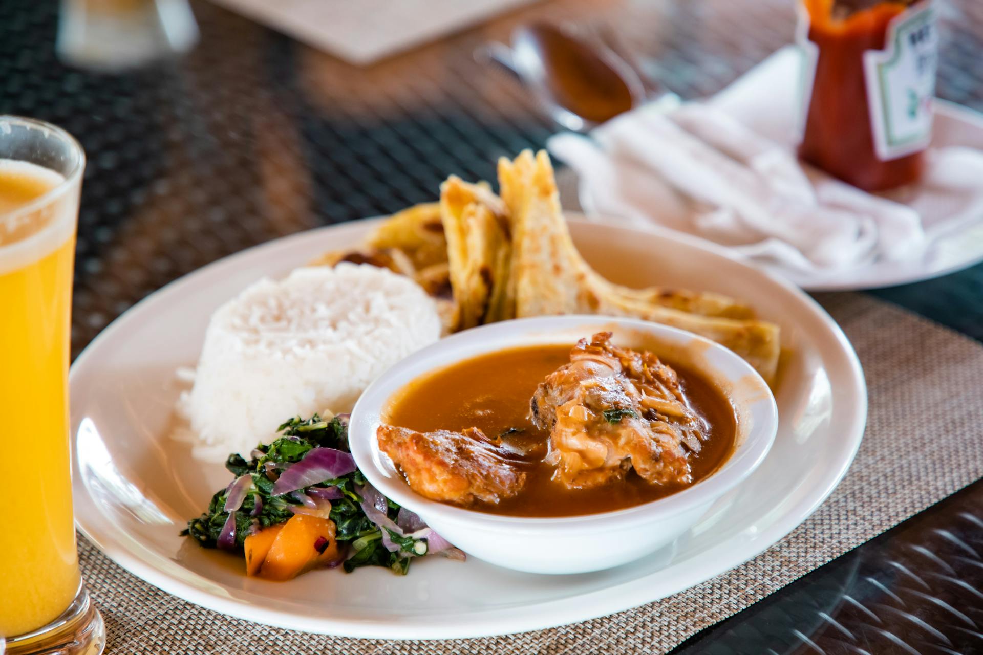 Delicious traditional Ugandan meal featuring rice, stew, greens, and chapati on a dining table.