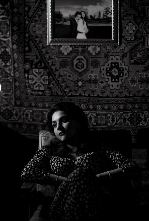 Free Elegant black and white portrait of a woman seated, with intricate wall tapestry. Stock Photo