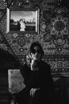 A woman in sunglasses and headscarf poses in a vintage black and white interior.