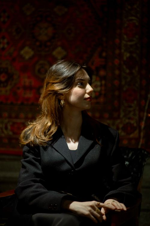 Free Portrait of a woman in a black blazer, sitting indoors, under warm light. Stock Photo