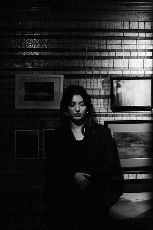 Free Moody black and white portrait of a woman standing against an art-lined wall. Stock Photo