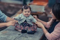 可爱的婴儿坐在桌子上，父母在室内牵着手，微笑着