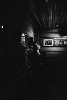 Moody black and white photo of a woman in a shadowy interior setting.