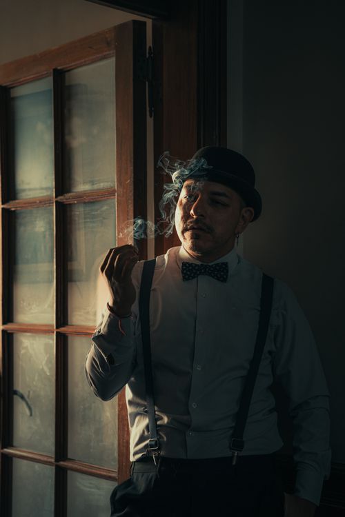 Free A well-dressed man in a bowler hat smoking, captured in stylish light. Stock Photo
