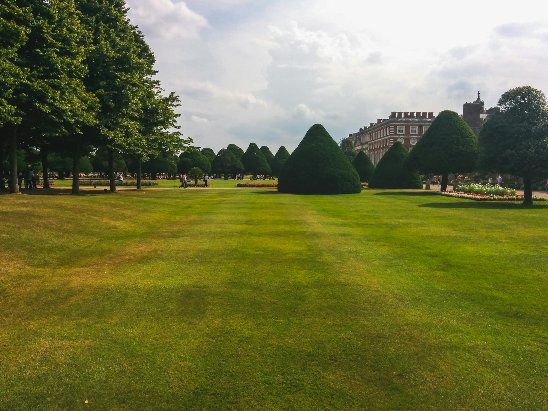 Beautiful landscaped garden with topiary near a historic mansion, under a cloudy sky.