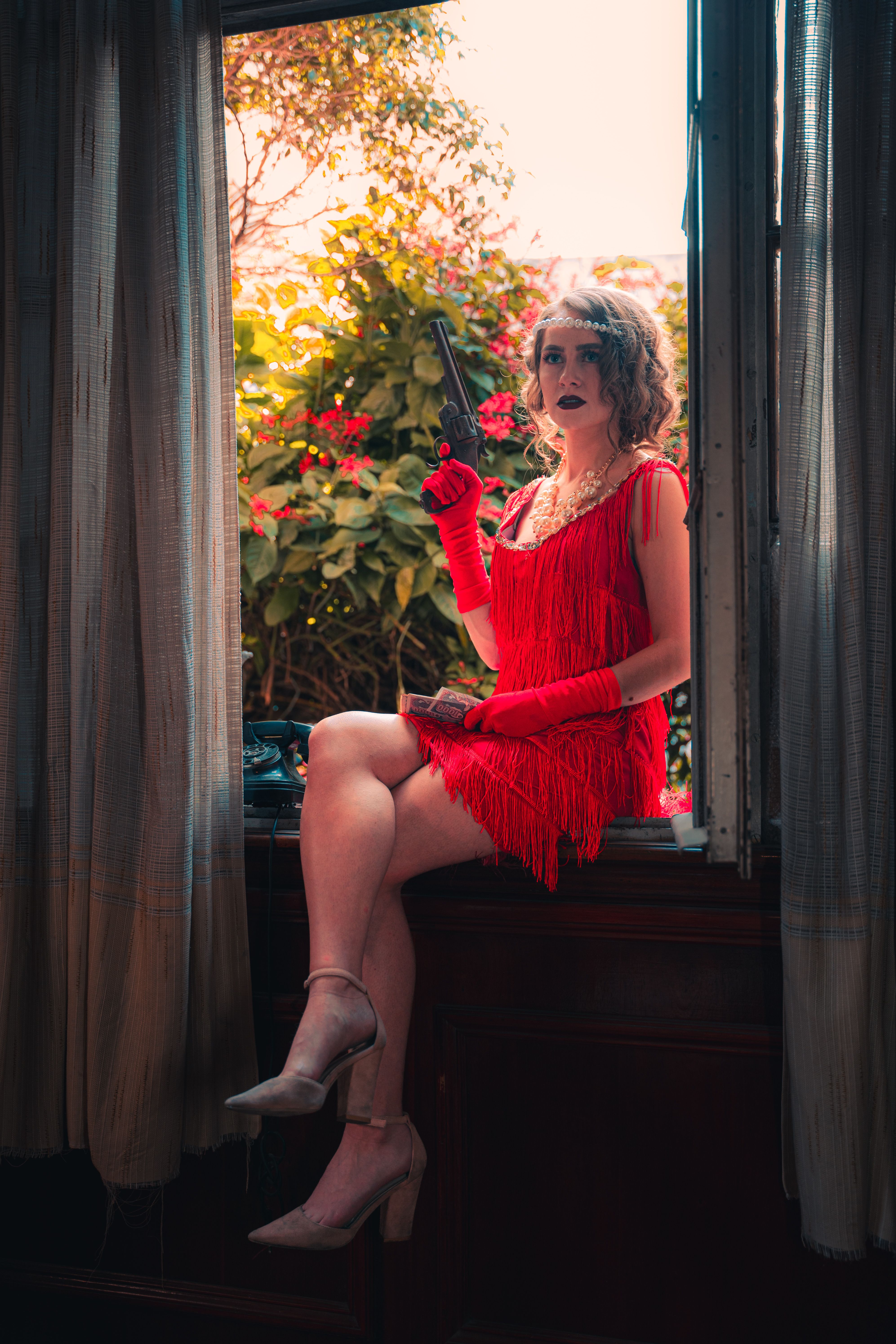A stylish woman in a red flapper dress sits elegantly holding a cigarette holder.