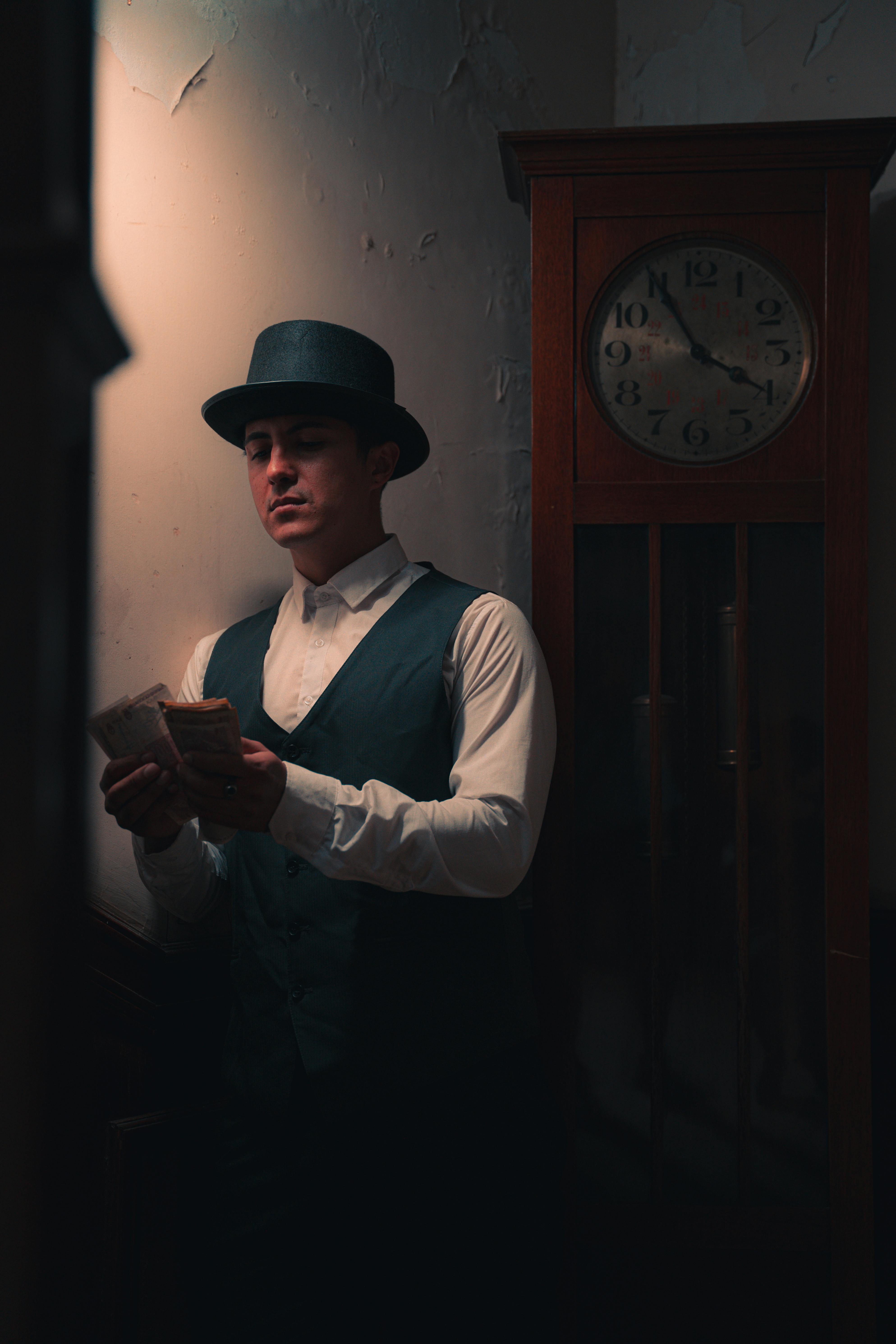 A man in vintage attire counts money by an old clock, evoking a classic mafia style.
