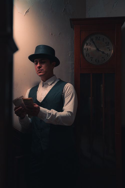 Free A man in vintage attire counts money by an old clock, evoking a classic mafia style. Stock Photo