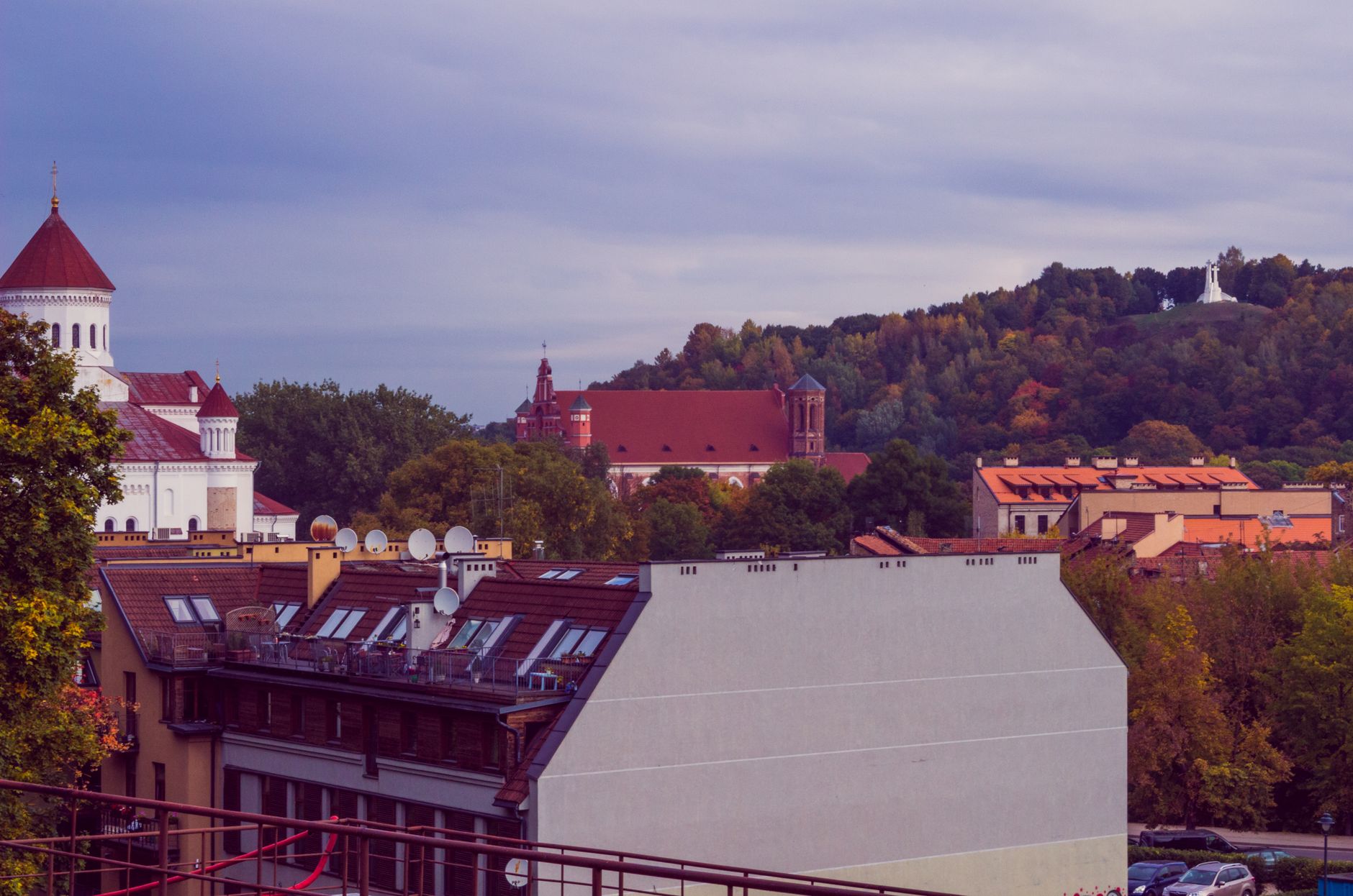Charming view of Vilnius with historic buildings and lush hills under a cloudy sky.