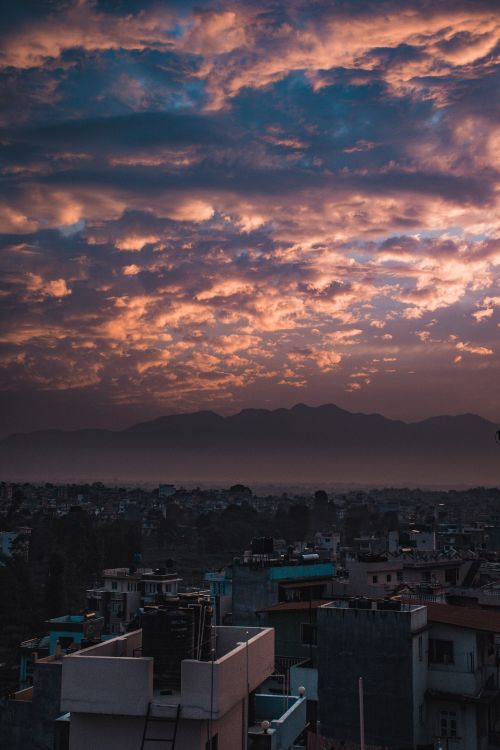 Free A breathtaking view of a city skyline under dramatic evening clouds with a mountain backdrop. Stock Photo