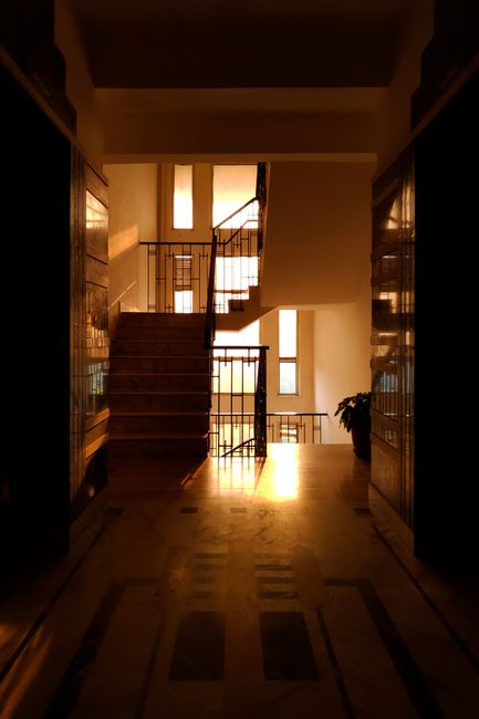 A hallway with stairs basked in golden sunset light inside a New Delhi building.