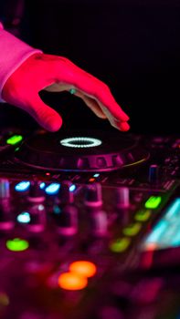 Close-up of a DJ's hand mixing music in a vibrant club setting under colorful lights.