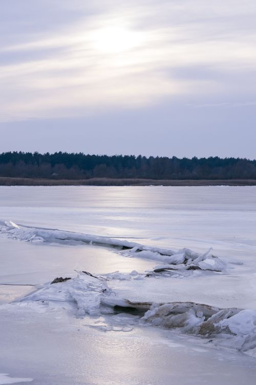 Free A tranquil winter landscape featuring a frozen lake with ice formations against a forest backdrop. Stock Photo