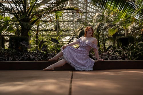 A woman in a purple dress sitting on a bench in a greenhouse