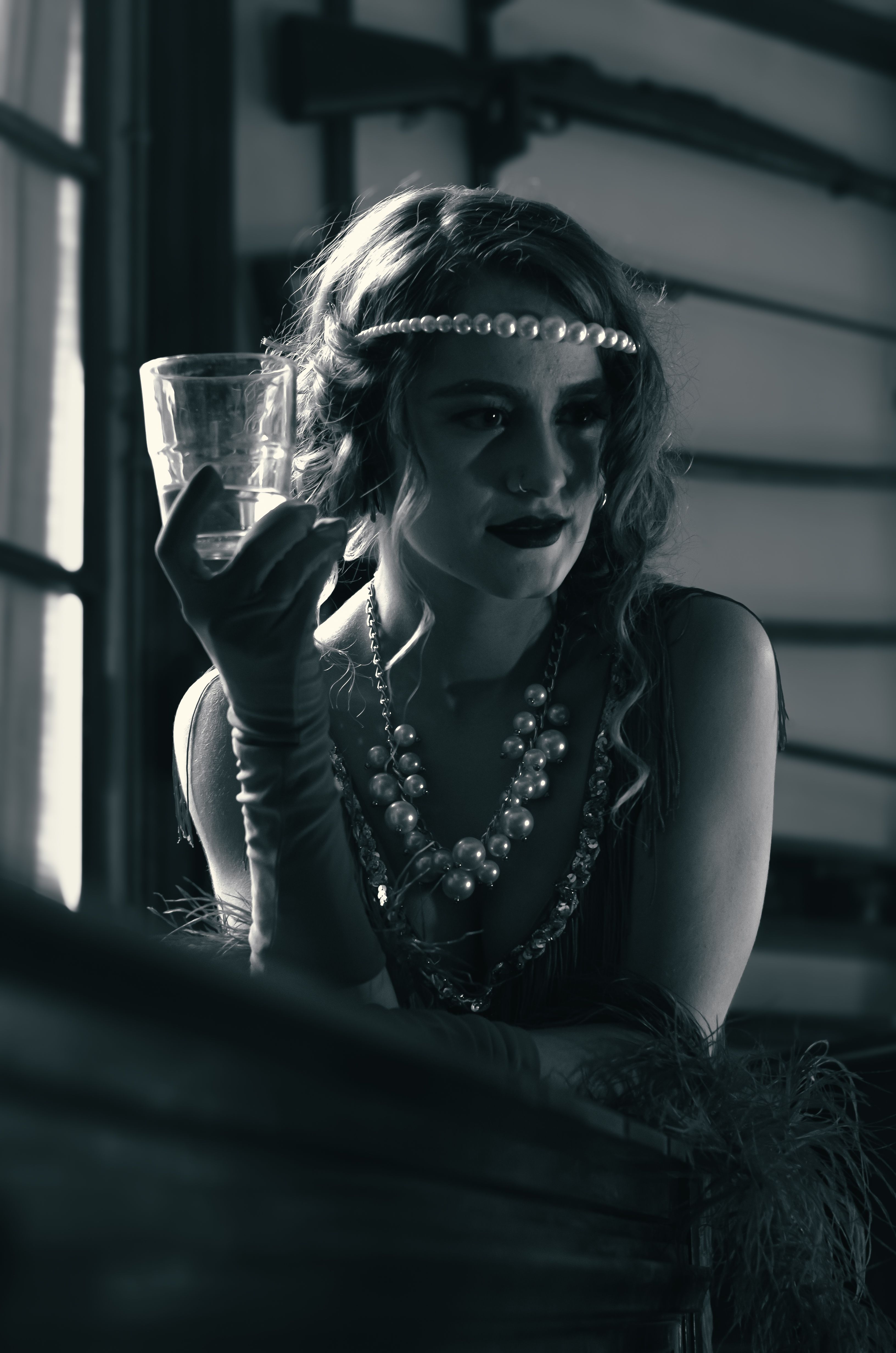 A woman in 1920s attire holding a glass, styled in black and white photography.