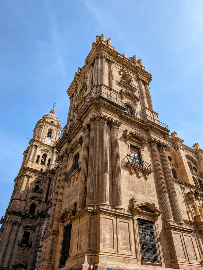 Baroque facade and bell tower of Málaga Cathedral under a blue sky