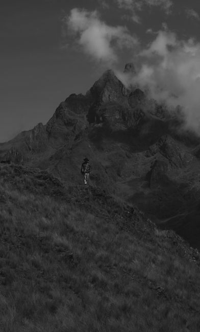 Fotomural Un senderista solitario asciende por una empinada ladera de montaña bajo una dramática cobertura de nubes.
