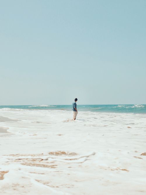 Free A man stands on a sunlit beach, surrounded by the gentle waves of the ocean, exemplifying relaxation and summer vibes. Stock Photo