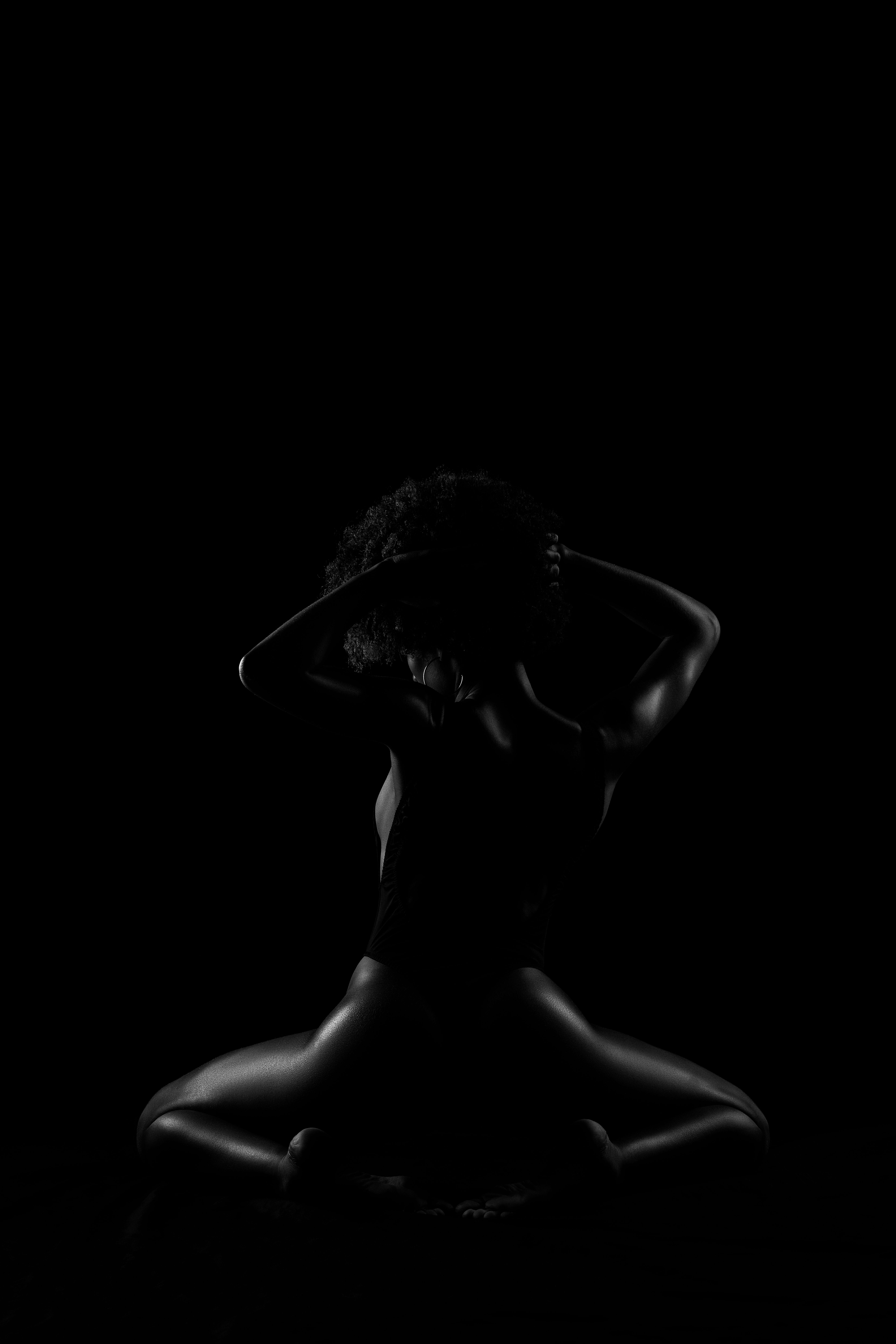 A person standing in low light with hands behind their head, conveying introspection and emotional vulnerability.