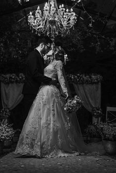 A couple sharing a romantic kiss under a chandelier at their wedding.