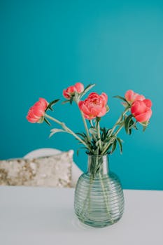 A stunning arrangement of vibrant pink roses in a ribbed glass vase against a teal backdrop, showcasing minimalist interior design.