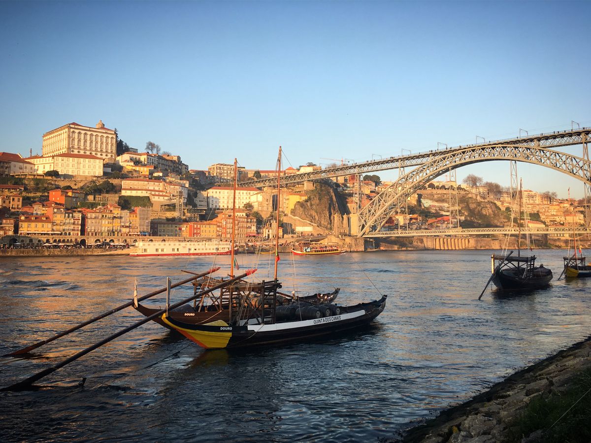Flat-bottomed rabelo boats moored under the Dom Luís I Bridge, the hillside of Porto stacked up behind them gone amber in the last low light.
