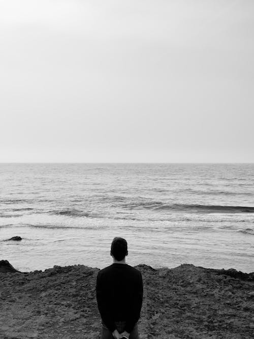A man is sitting on the beach looking out to the ocean