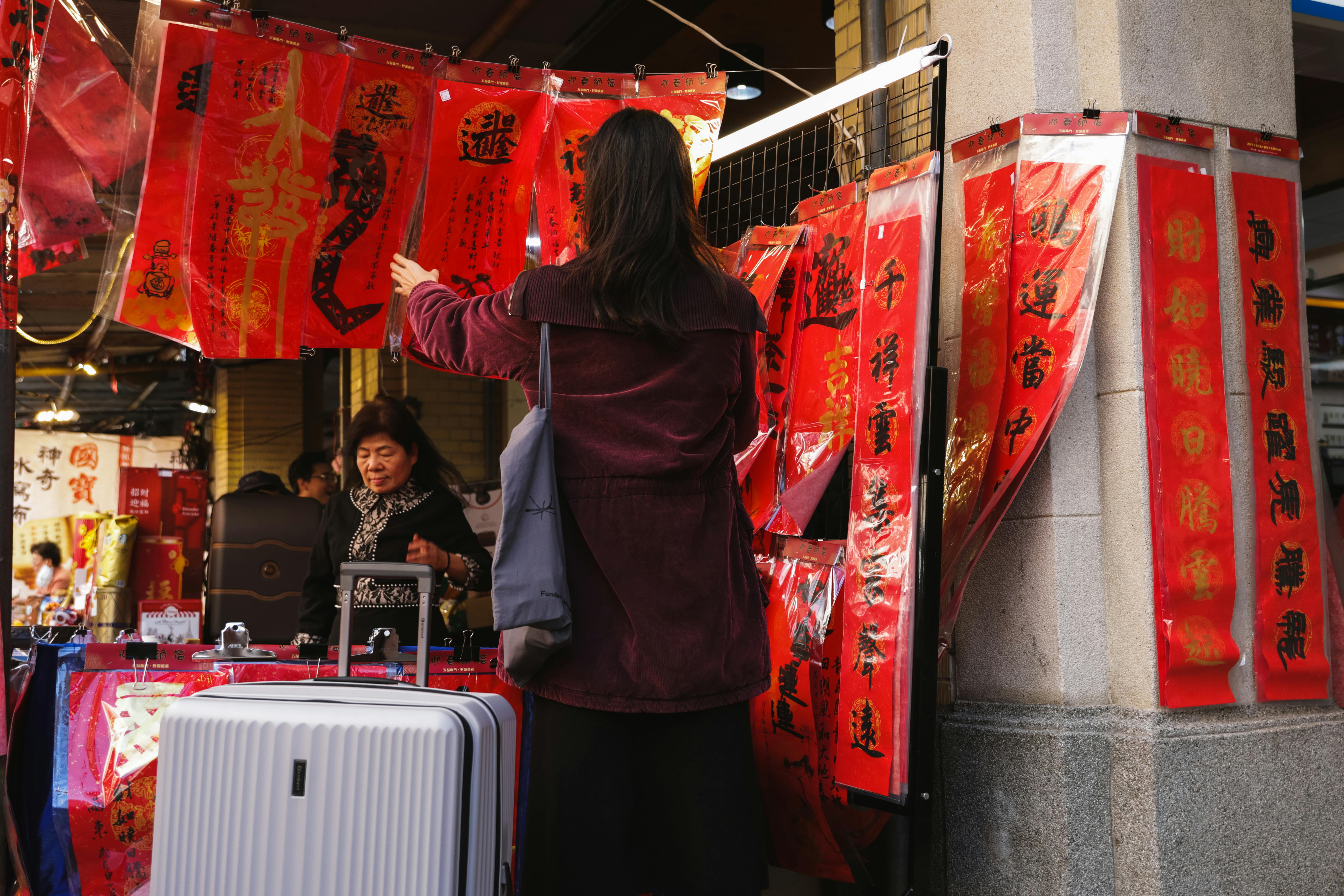 Women shopping at an Asian street market with vibrant red banners during the day.
