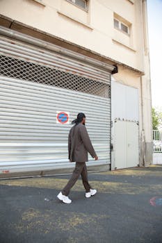 A professional in a suit walks past an industrial building's shuttered entrance.