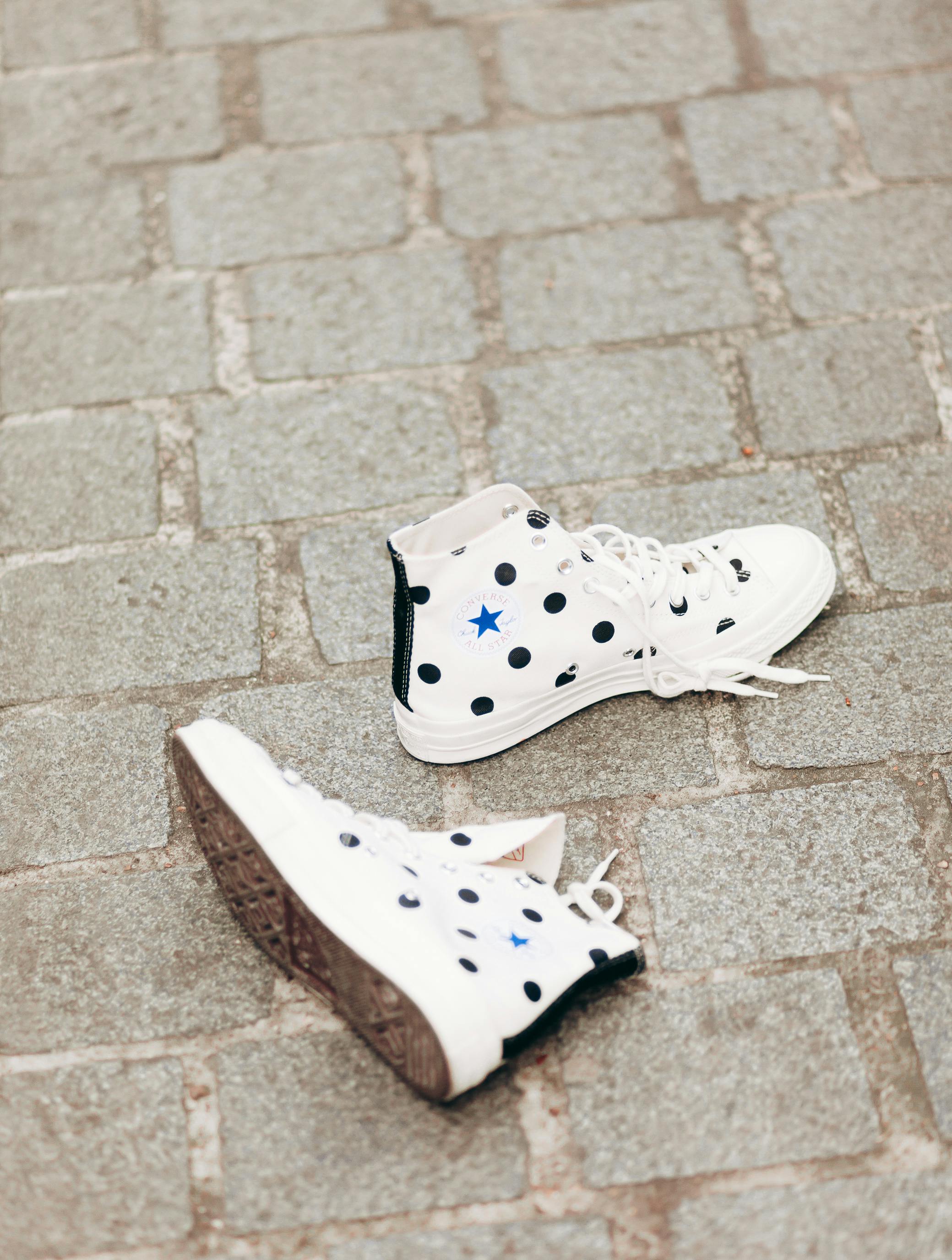 Stylish white sneakers with polka dots laid on a cobblestone pavement outdoors.
