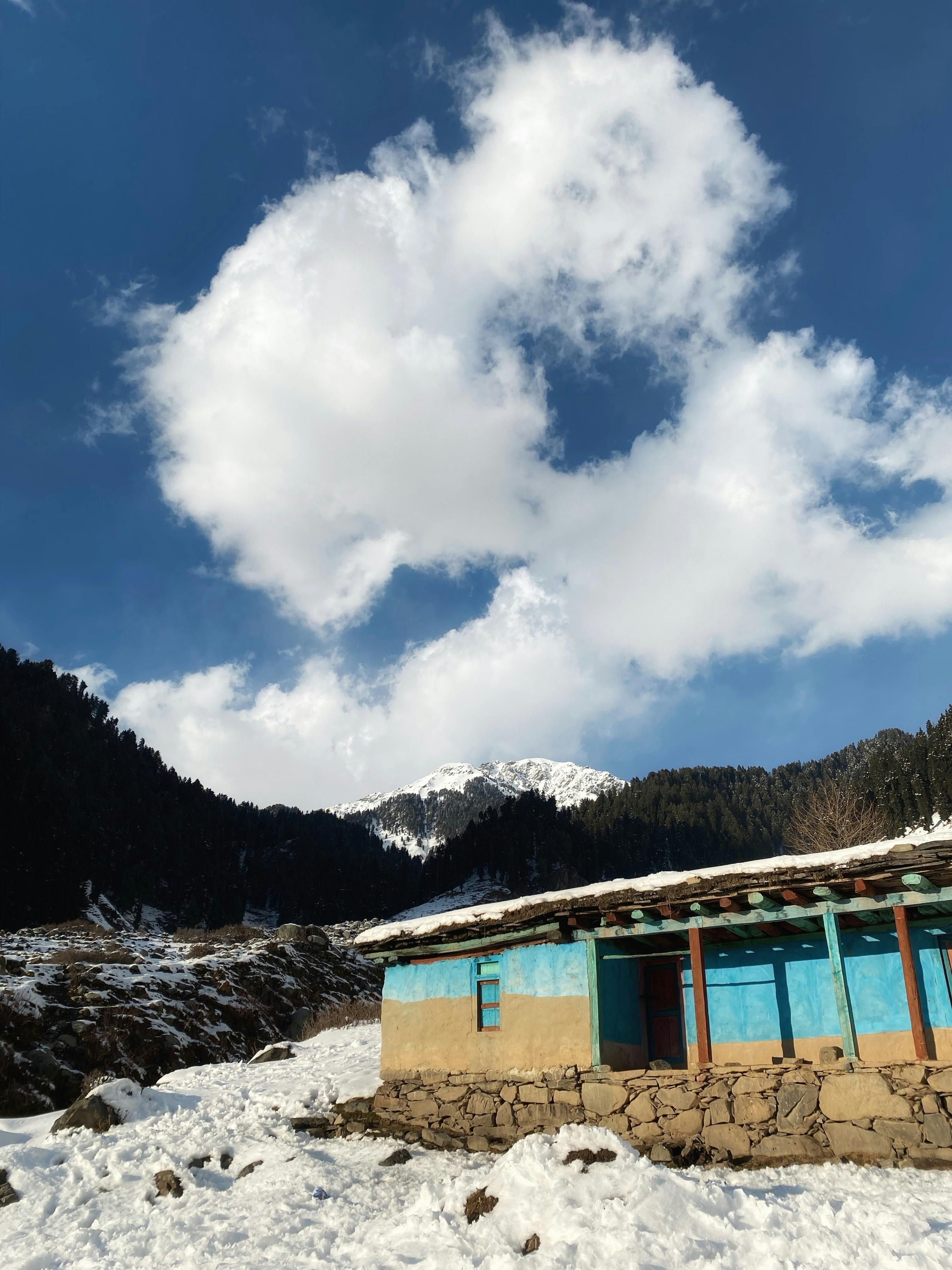A picturesque snow-covered house in a mountainous winter landscape under a clear blue sky.