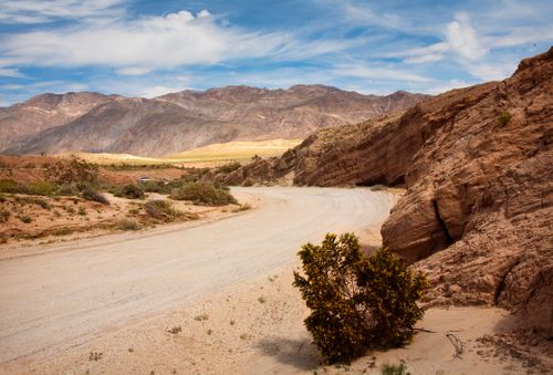 Free A winding road through Borrego Springs' arid desert landscape beneath a blue sky. Stock Photo