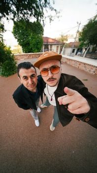 Two stylish men posing outdoors in İstanbul with a playful, modern vibe.